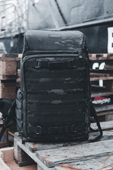 A durable black backpack rests on wooden pallets in an industrial outdoor setting.