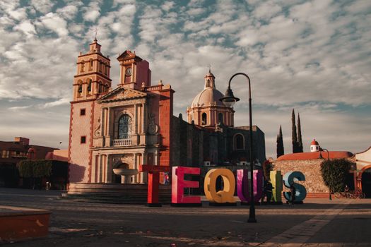 Charming town square in Tequisquiapan, Mexico, featuring a historic cathedral under a cloudy sky.