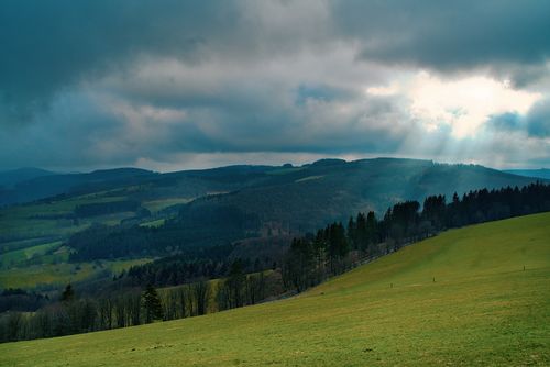 Free A breathtaking view of green hills under dramatic clouds with sunlight breaking through. Perfect for nature lovers. Stock Photo