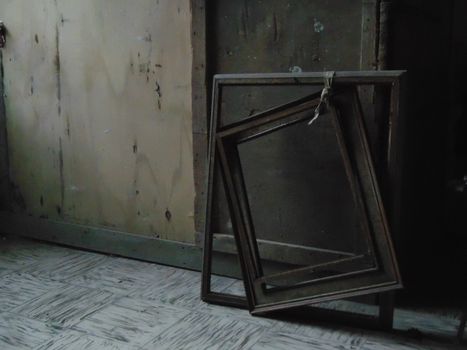 Old wooden painting frames leaning against a faded wall in an abandoned room.