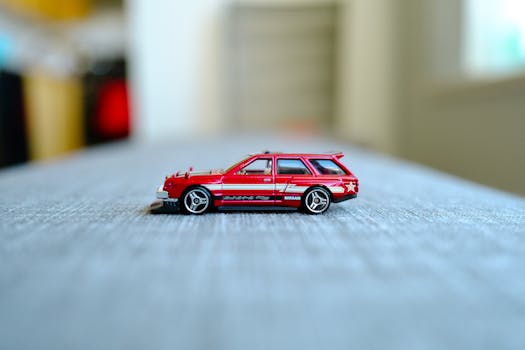 A sleek red model car on a textured grey desk in a modern office setting.
