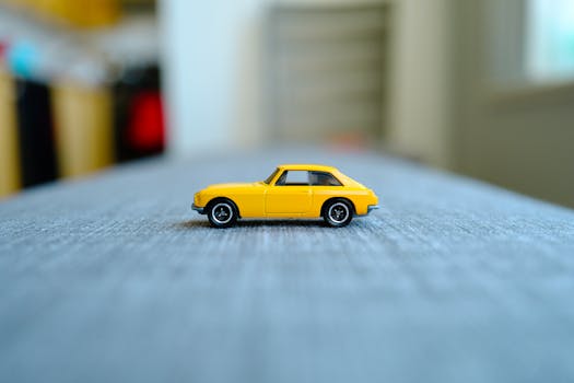 Close-up of a yellow toy car on a textured surface with blurred background indoors.