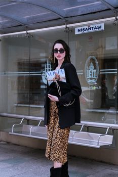 Stylish woman in sunglasses standing in Nişantaşı, Istanbul holding a fashion magazine.