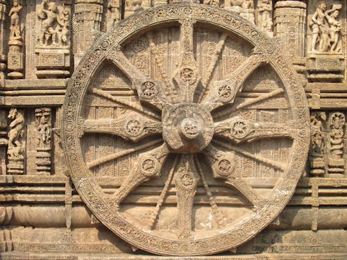 A large wheel is on the side of a stone building