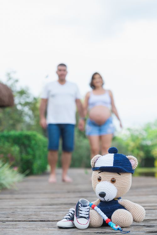 Free Blurred pregnant couple holding hands with baby shoes and teddy bear in foreground. Stock Photo