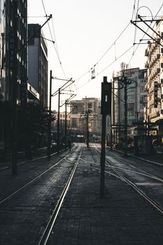 An empty urban street with tramway tracks at dawn, modern buildings lining the road.