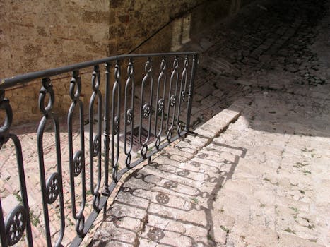 Sunlit historic stone staircase with intricate iron railing casting shadows.