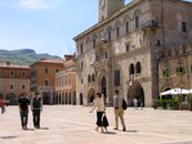 Charming view of Piazza del Popolo in Ascoli Piceno, Italy, featuring medieval architecture and lively atmosphere.