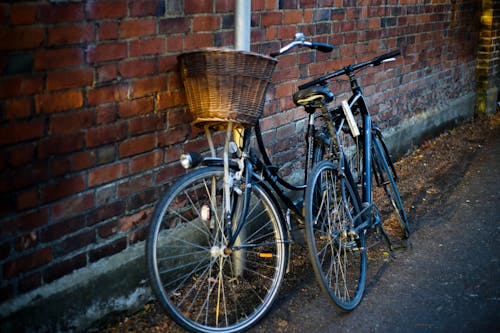 무료 두 개의 검은 자전거가 붉은 벽돌로 덮인 건물 옆에 세워져 있습니다. 스톡 사진