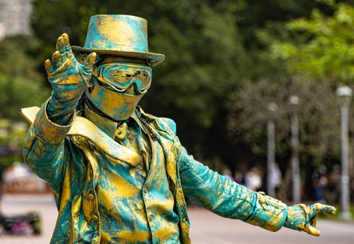 A striking street performer in a vibrant gold and blue statue-like costume posing outdoors.