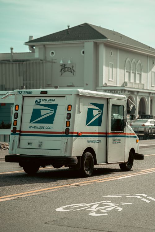 Free USPS delivery truck driving on a street in Sausalito, CA with an urban backdrop. Stock Photo