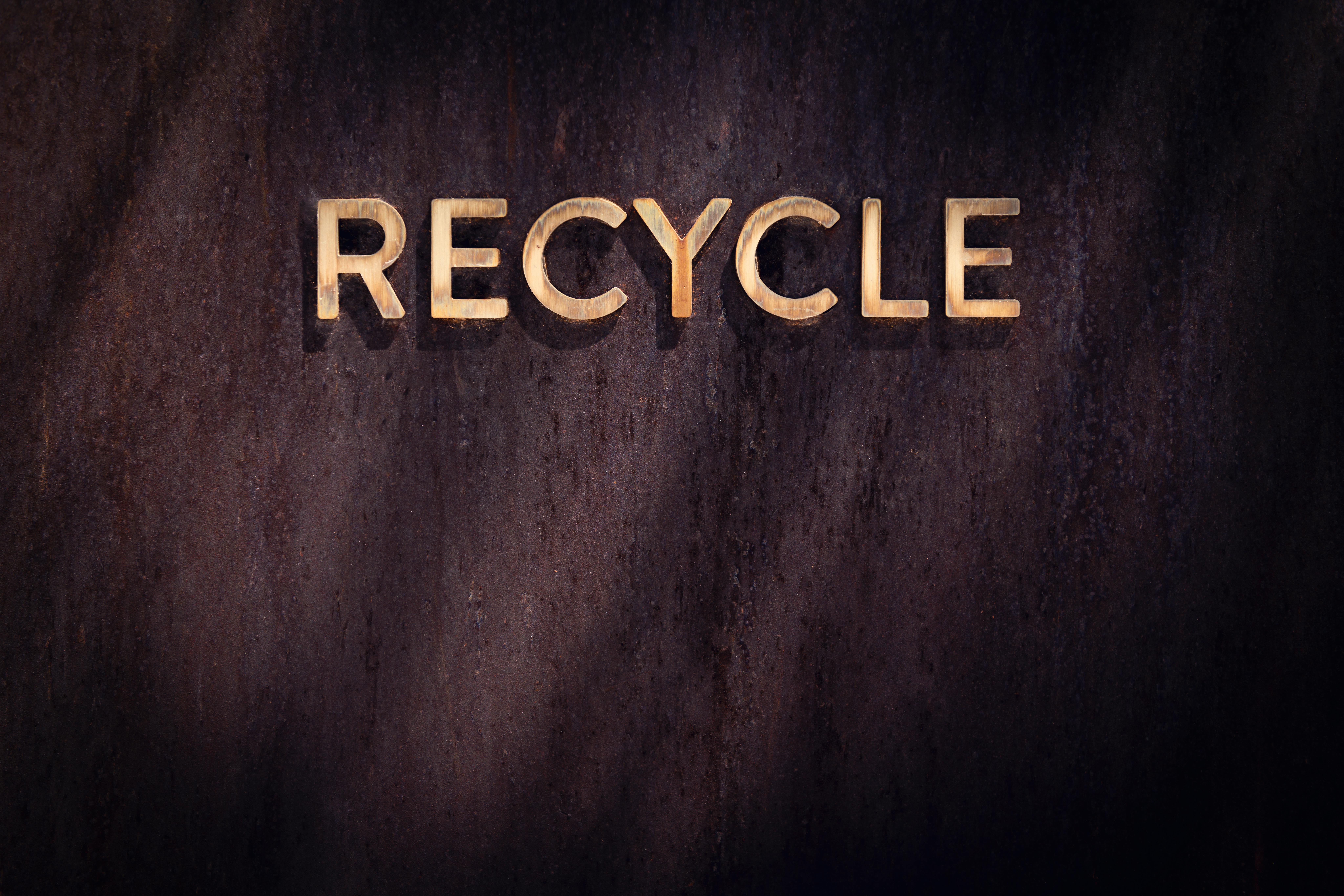 Golden "Recycle" sign on a rustic wood wall, highlighting eco-friendly concepts.
