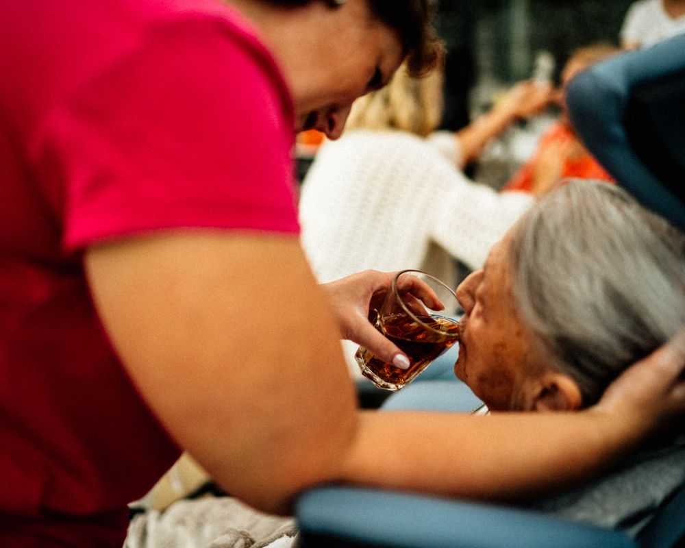 Caregiver helping an elderly woman drink tea, demonstrating compassionate social care