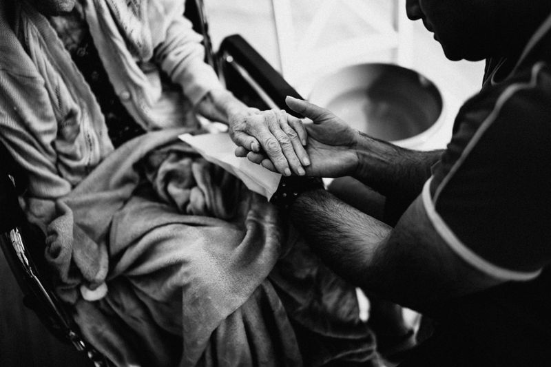 Caregiver holding elderly patient's hands — black and white