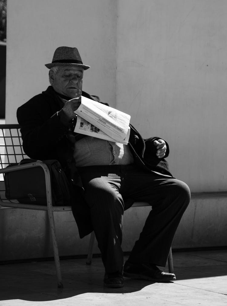 Senior Man Reading A Newspaper On A Bench