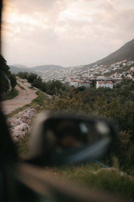 Capture of a rural town with tree-lined roads, mountains, and buildings on a cloudy day.