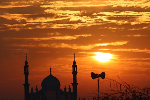 Silhouetted mosque with spires at sunset under a vibrant orange sky, showcasing religious architecture.