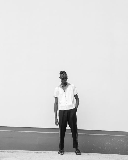 Trendy man in sunglasses and white shirt posing casually against a white wall.
