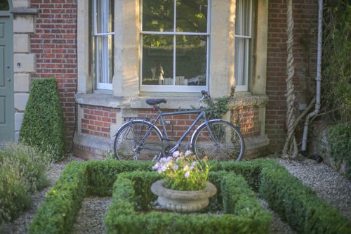 Free A bicycle leans against a brick house with a lush garden, ideal for serene outdoor living. Stock Photo