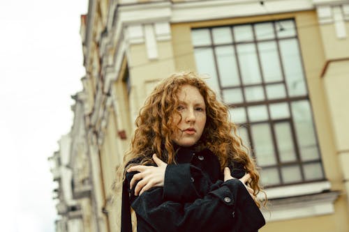 Young Woman with Curly Hair Standing in front of a Building in City 