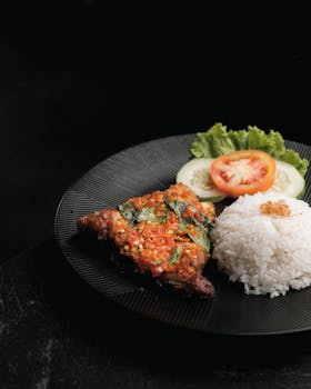 Delicious grilled beef served with rice, cucumber, tomato, and lettuce on a black plate.