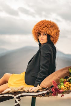 Stylish woman posing outdoors in a hat and yellow skirt against a mountain backdrop.