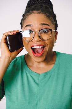 Excited woman in glasses talking on a smartphone with a surprised expression.