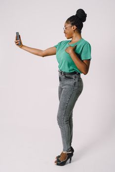 Smiling woman taking a selfie in a studio with a white background and stylish outfit.