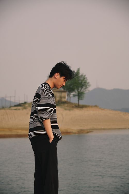 Free Teenager standing by the sea, hands in pockets, in a serene beach setting. Stock Photo
