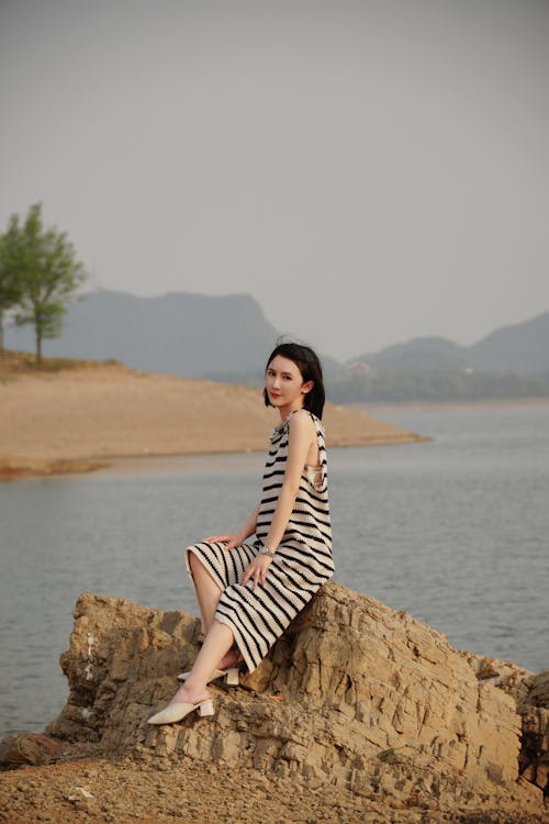 Young Woman in Striped Dress Sitting on a Rock