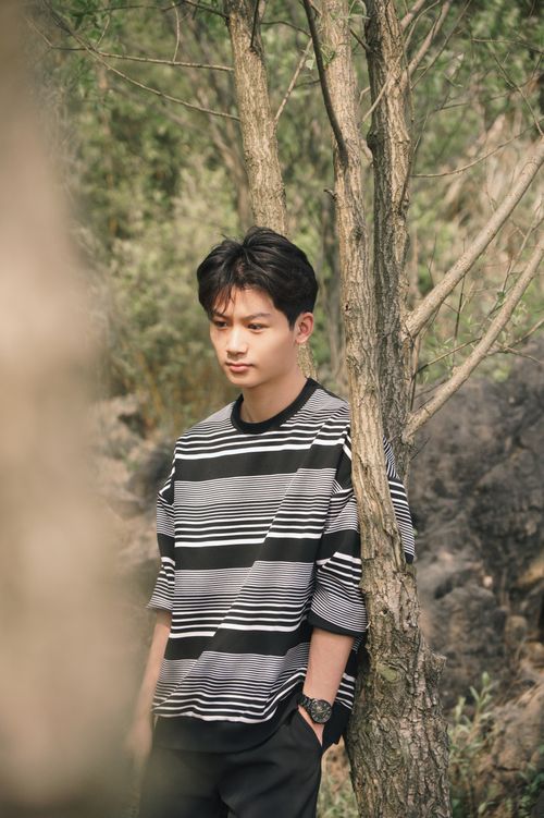Free Portrait of a young man in a striped shirt standing among trees outdoors. Stock Photo