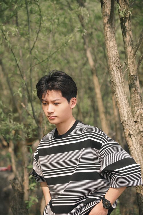 Free Youthful portrait of a teenager standing in a serene forest wearing a striped sweater. Stock Photo