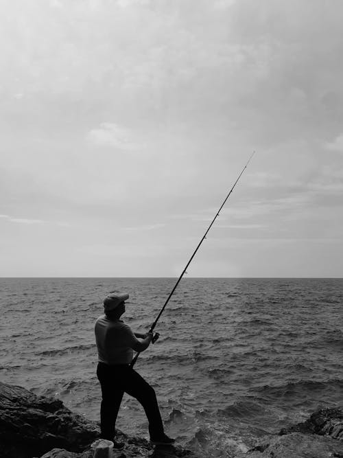 Black and White Photo of a Fisherman Standing on the Seashore
