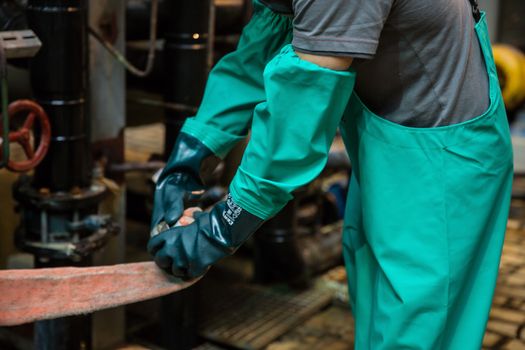 A worker wearing protective clothing operates machinery in an industrial setting, focusing on safety.