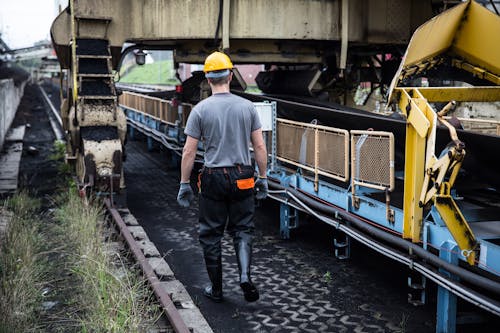 Back View of a Worker Wearing a Helmet, Walking by a Machinery