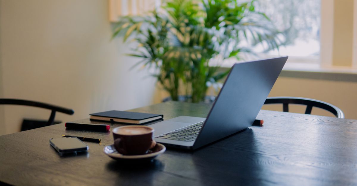 A warm, inviting workspace in Amsterdam featuring a laptop, coffee, and potted plant.