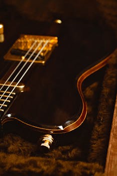 Detailed view of an electric guitar with dark tones and golden accents, highlighting strings and body.