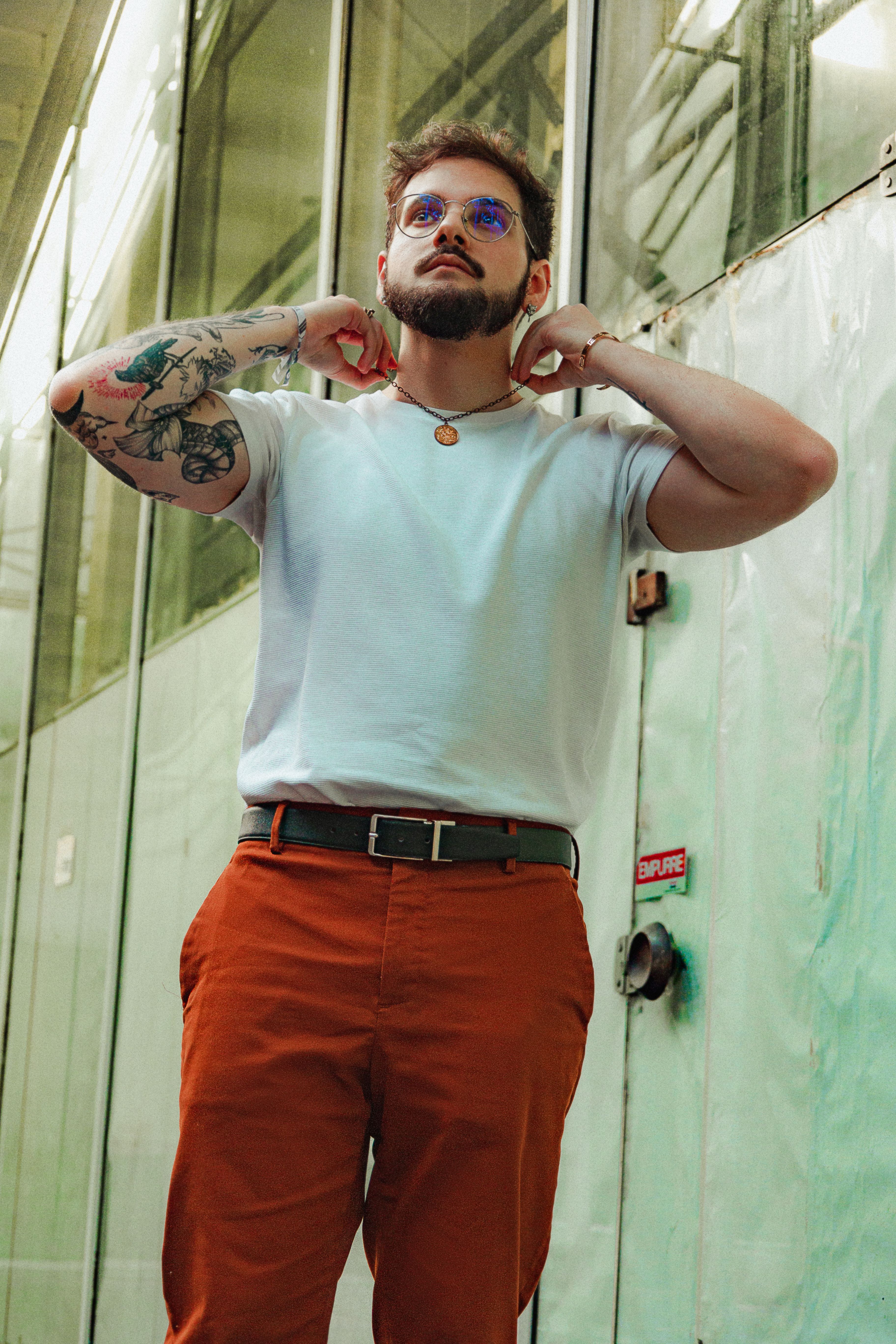 Portrait of a stylish bearded man with tattoos posing confidently indoors next to a glass wall.
