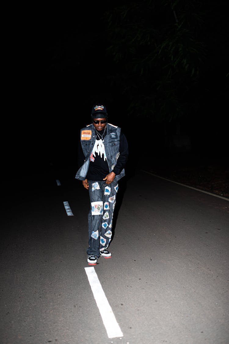 Night Photo Of A Young Man Walking Down The Street Wearing Blue Jeans And A Denim Vest