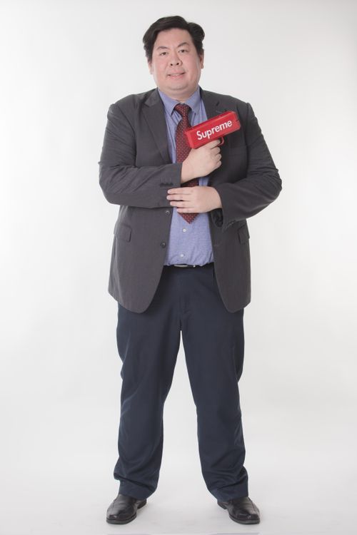 Free Asian man in a suit holds a red toy gun against a white background. Stock Photo
