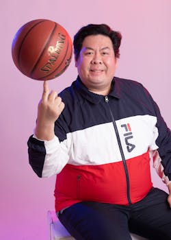 Smiling man in sports attire spinning a basketball on his finger indoors.