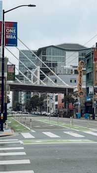 A city street featuring modern architecture and a unique suspended bridge.