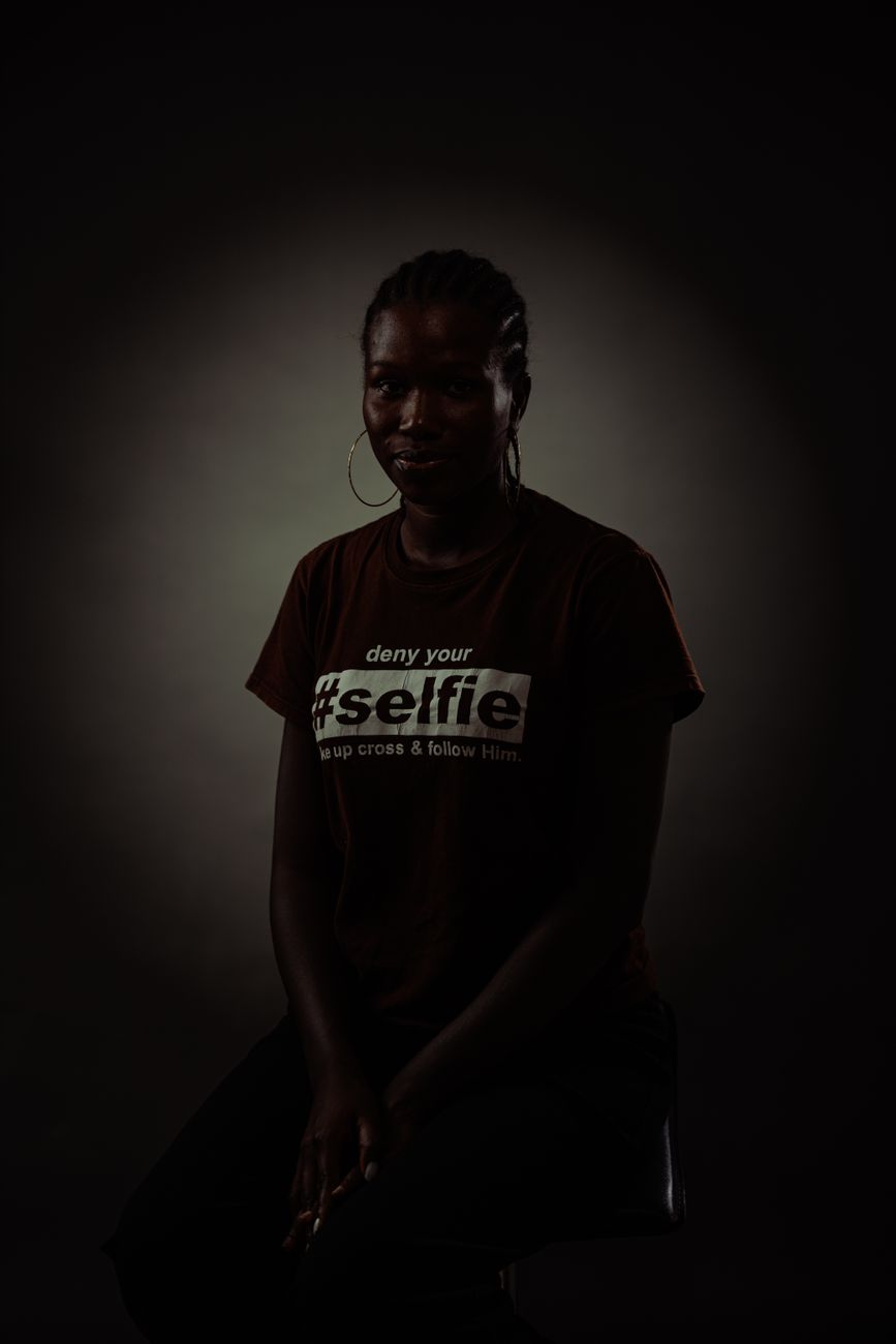 Artistic studio portrait of a young woman in shadows wearing a graphic tee.