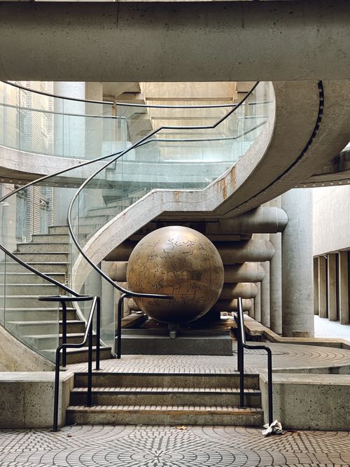 Free Elegant spiral staircase enveloping a bronze globe sculpture in a contemporary urban setting. Stock Photo