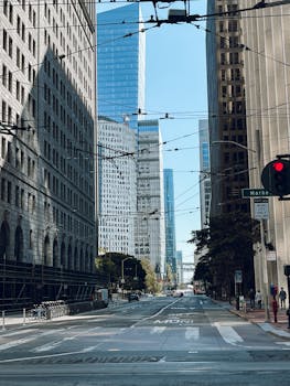 A bustling urban street flanked by tall modern skyscrapers under a clear blue sky.