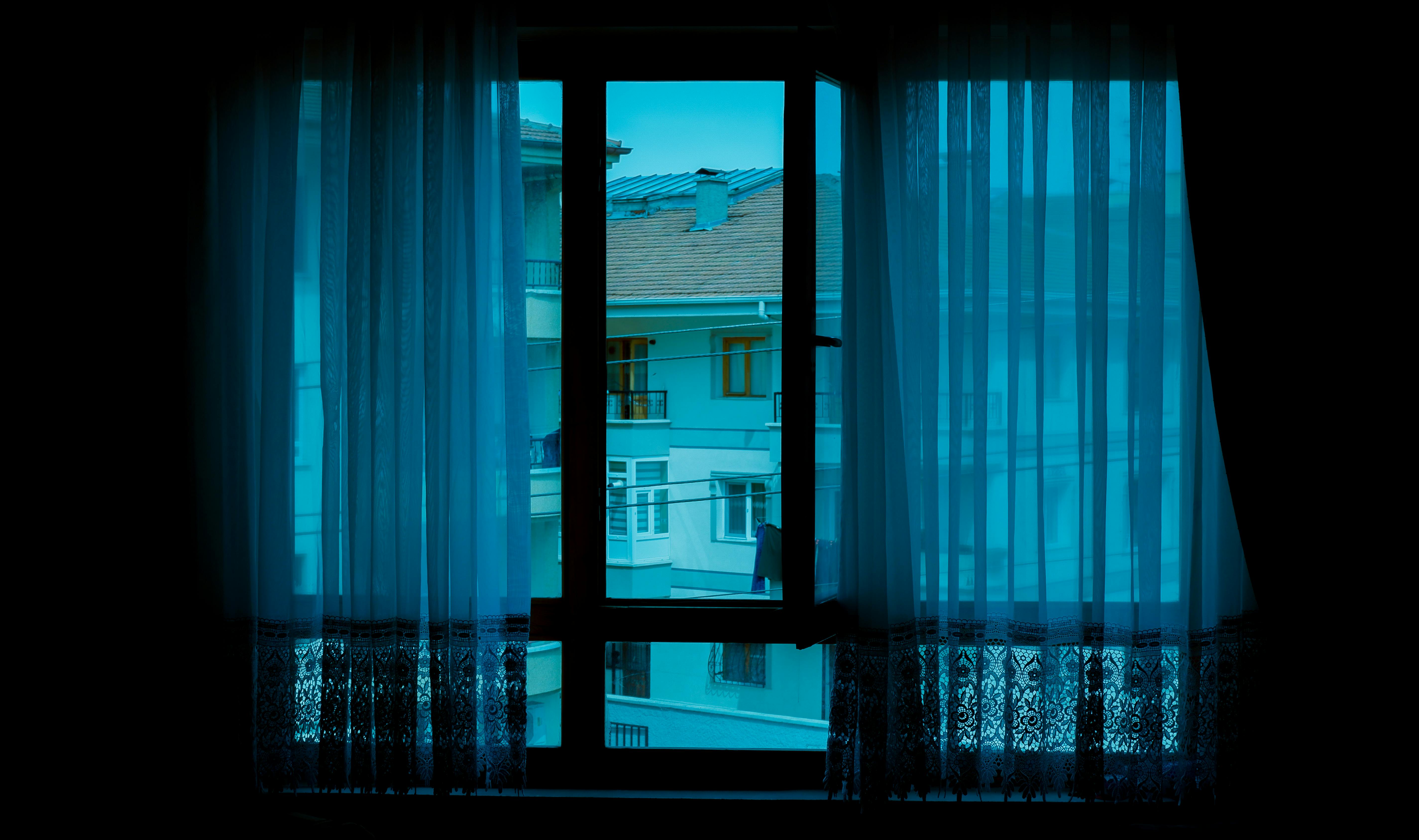 View of adjacent apartment buildings through a window with sheer curtains, creating a tranquil urban scene.