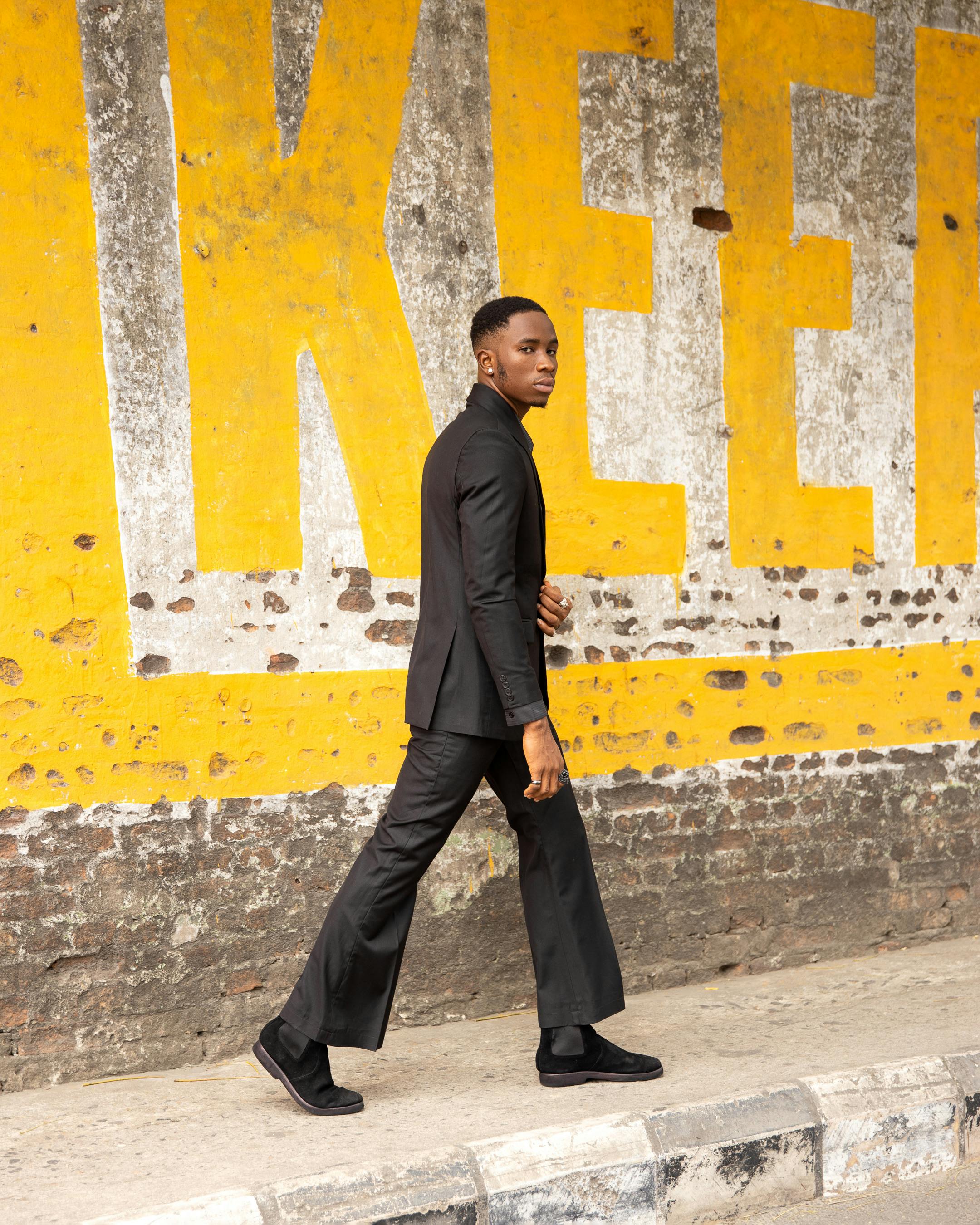 Black man in a suit walks by a vibrant yellow wall on the streets of Lagos, Nigeria.