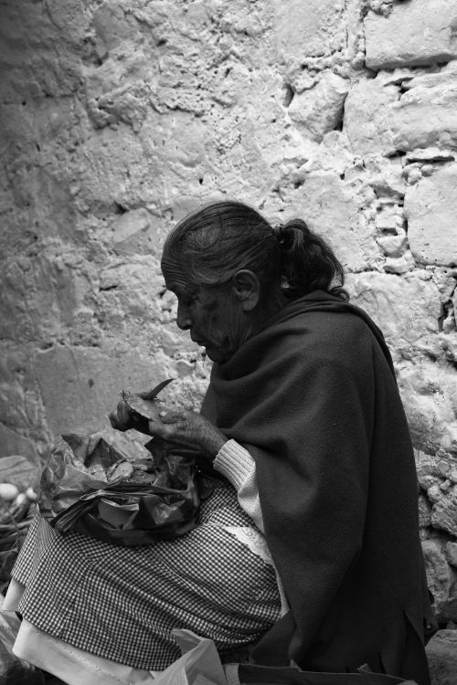 Free Black and white portrait of an elderly woman preparing food against a rustic wall. Stock Photo