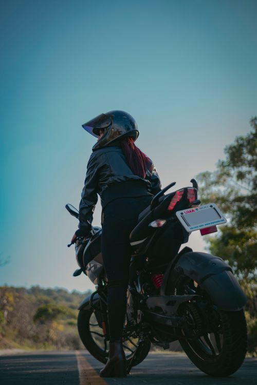 Free Female motorcyclist in protective gear riding through a scenic road on a bright day. Stock Photo