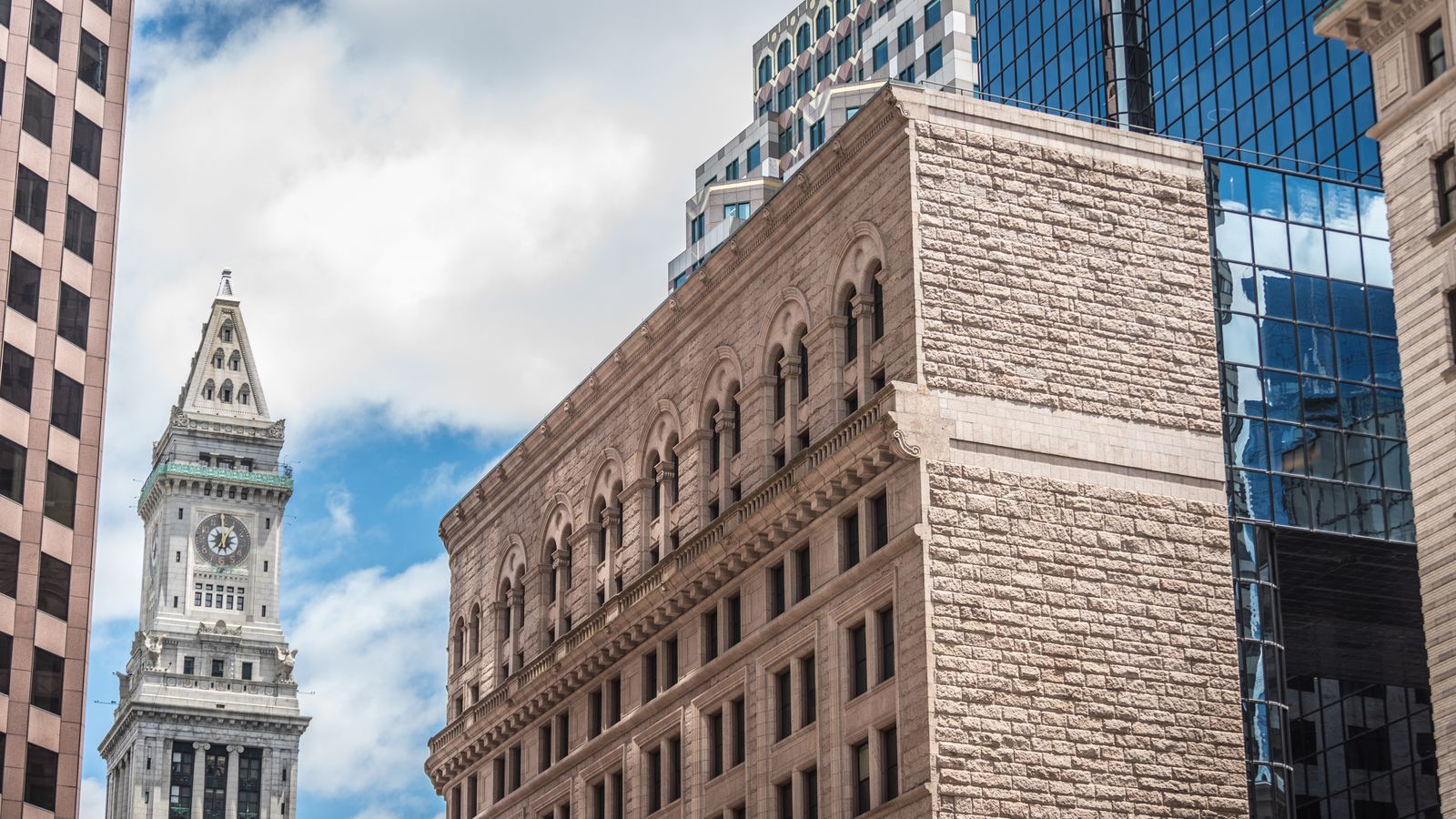 A striking view of Boston's Custom House Tower and surrounding skyscrapers against a bright sky.